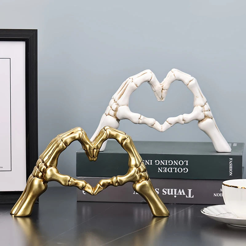 Two heart-shaped sculptures, one gold and one white, on a surface with books in the background.