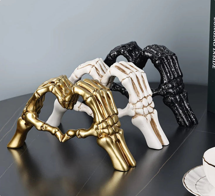 Three decorative hand sculptures in gold, white, and black on a reflective surface.