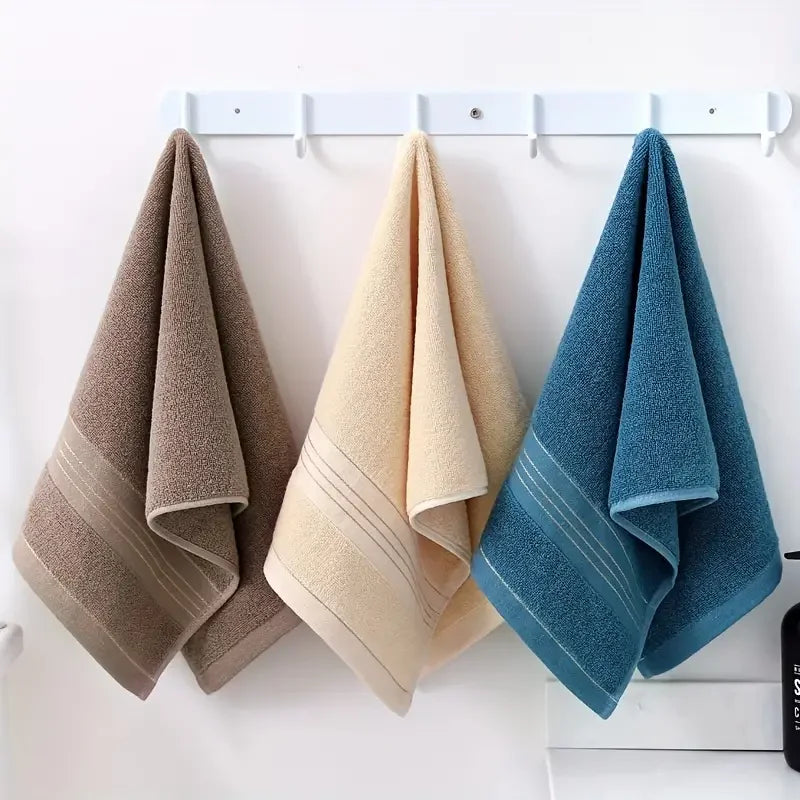 Three towels in brown, beige, and blue hanging on a white rack against a white wall.